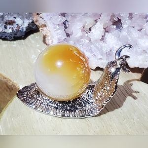 Snail shaped metal sphere holder with carnelian sphere